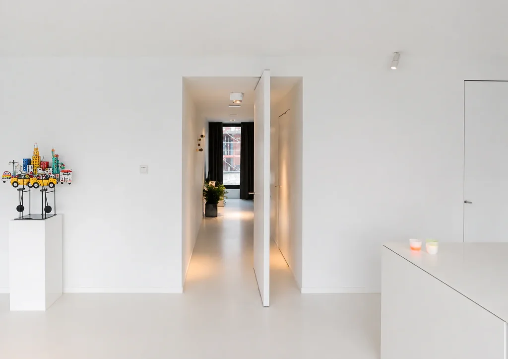 Concealed white pivot door opening onto a long hallway in a white interior