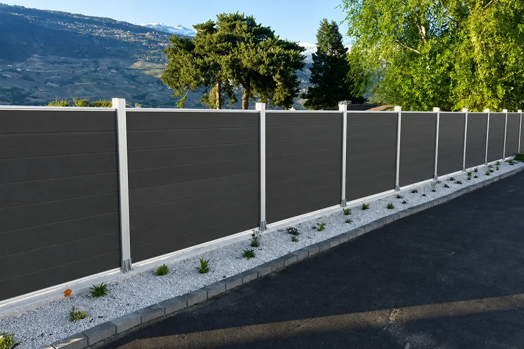 Long dark gray composite fence with white posts along a road
